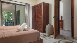 Ein Schlafzimmer mit einem Bett, einem Holzschrank, einem großen Fenster und Blick ins Grüne.