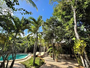 Un espace piscine agrémenté de chaises longues, entouré de diverses plantes et arbres tropicaux.