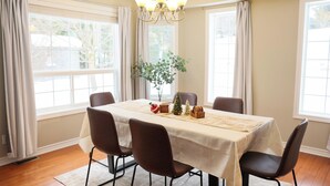 A dining room with a table set for four, surrounded by chairs, a chandelier, and a window with curtains.