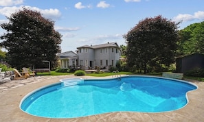 Una piscina residencial con una casa al fondo.
