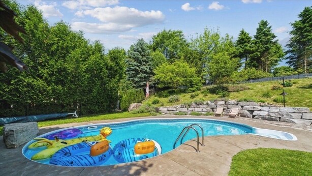 A swimming pool with inflatable toys, surrounded by a stone wall and greenery.