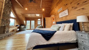 Un dormitorio de cabaña de madera con una cama, mesitas de noche, una pared de piedra y un ventilador de techo.