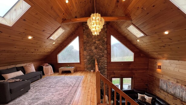 Un loft amplio con interior de madera, una pared de piedra, una lámpara de araña y vistas al exterior.