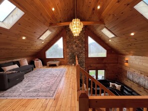 A spacious loft with a wooden interior, a stone wall, a chandelier, and a view of the outdoors. - Remote Cabin near Knoebel’s (Catawissa)