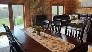 Un interior de madera con chimenea de piedra, sofá de cuero, mesa de comedor con sillas y una araña.