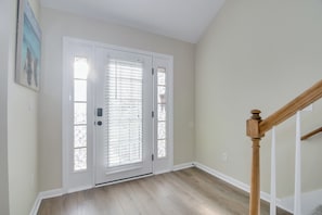 A hallway with a wooden floor, a white door with glass panels, and a wooden staircase. - North Augusta Coastal Home Near Golf, Trails & Events (North Augusta)