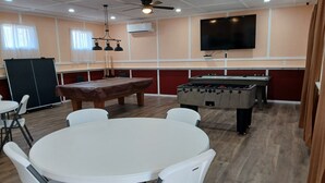 A room with a pool table, foosball table, and a television mounted on the wall. - RV #1 - 30 Amp - Serene campground in Graysville perfect for outdoor adventures (Graysville)