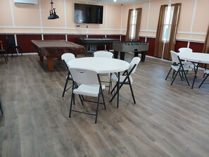 Una habitación con mesa de fútbol, televisor y sillas plegables.