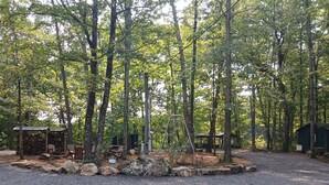 A campground with a gravel area, wooden structures, and tall trees. - RV #1 - 30 Amp - Serene campground in Graysville perfect for outdoor adventures (Graysville)