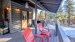 Une cabane en rondins avec un porche, deux fauteuils Adirondack rouges et une petite terrasse.