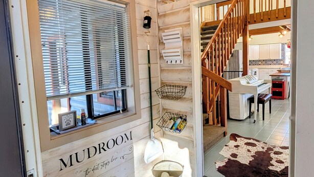 Un intérieur en bois avec une pancarte indiquant « LOCAL À CHAUSSURES », un escalier en bois, un piano et un tapis en peau de vache.