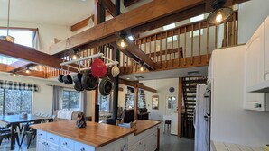 Une cuisine spacieuse avec un grand îlot central, des poutres en bois et des ustensiles de cuisine suspendus.