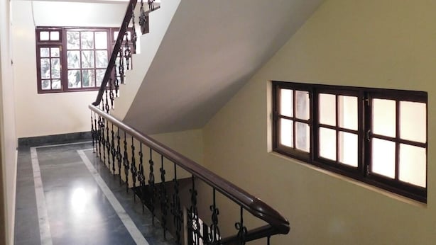 A staircase with a dark handrail and balusters, leading to a landing with a window. - OS HOTEL HIDDEN FLOWER (Gangtok)