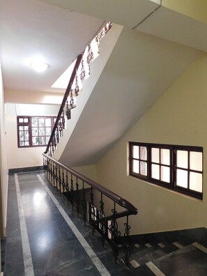 A staircase with a dark handrail and balusters, leading to a landing with a window. - OS HOTEL HIDDEN FLOWER (Gangtok)