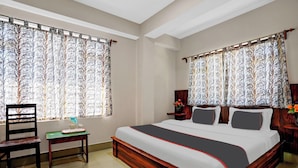 A bedroom with a large bed, two nightstands, a chair, and a small table. - OS HOTEL HIDDEN FLOWER (Gangtok)