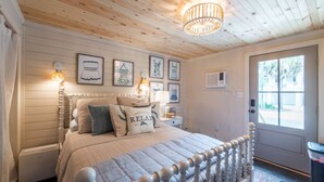 Ein Schlafzimmer mit Holzboden, einem Bett mit weißem Kopfteil, einem Nachttisch mit Lampe und gerahmten Bildern an der Wand.