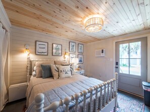 Un dormitorio con techo de madera, una cama con cabecera blanca, una mesita de noche con lámpara y cuadros enmarcados en la pared.