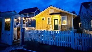 A two-story house with a white picket fence, a green door, and string lights on the porch.