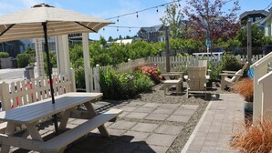 A patio area with picnic tables and chairs, a pergola with a striped canopy, and a white picket fence.