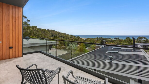 Ein Balkon mit zwei Stühlen, einer Holzwand und Blick auf das Meer und Bäume.