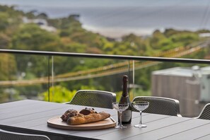 A table with a bottle of champagne, two glasses, and a plate of food on a balcony overlooking a green landscape. - Riptide Lorne (Lorne)