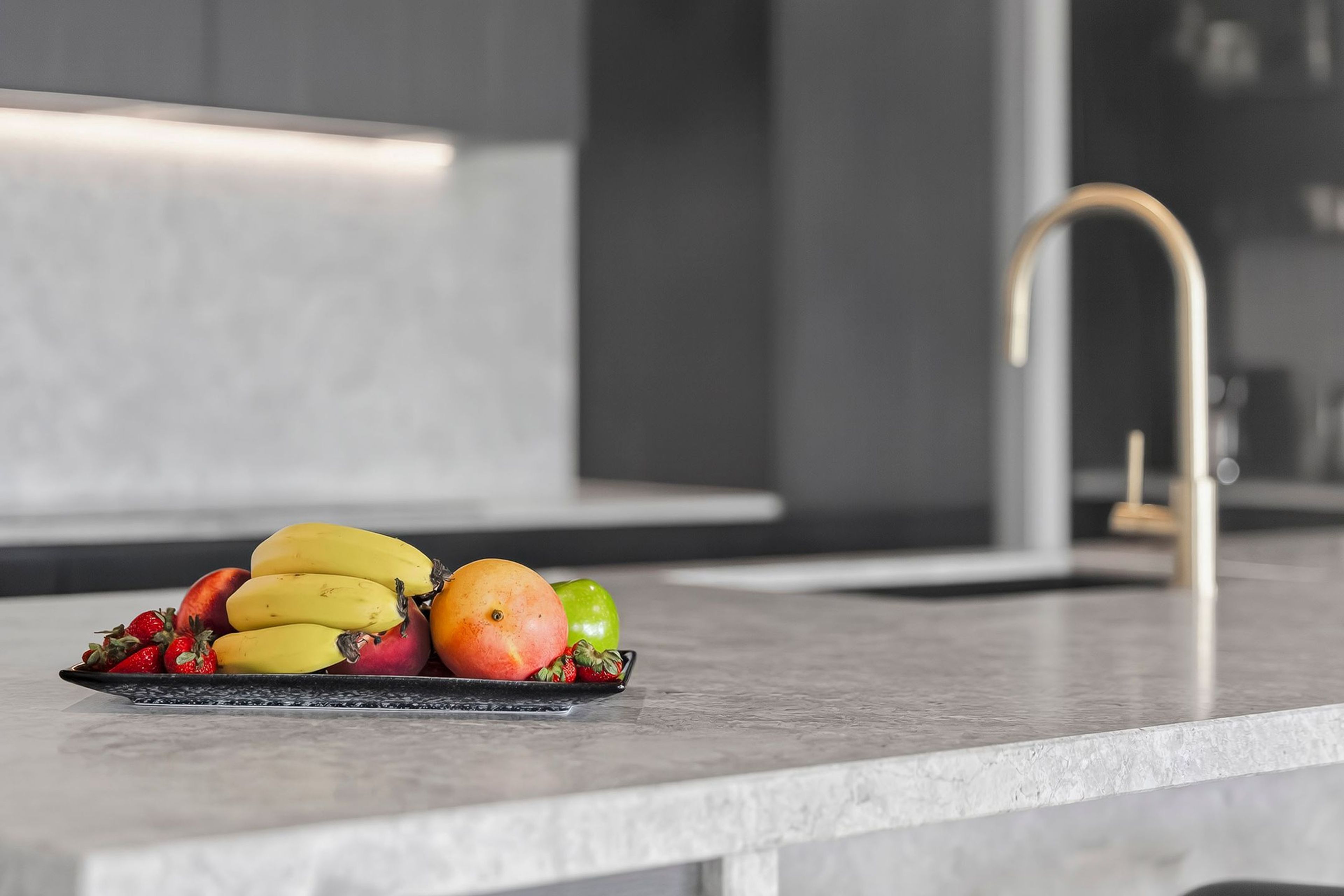 A kitchen counter with a fruit bowl containing bananas, apples, and strawberries.