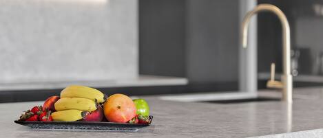 A kitchen counter with a fruit bowl containing bananas, apples, and strawberries.