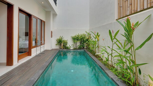 Un'area piscina moderna con un solarium in legno, porte in vetro e una rigogliosa vegetazione.