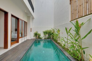 A modern pool area with a wooden deck, glass doors, and lush greenery. - Villa Taman Seminyak 27 - Seminyak (Seminyak)