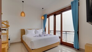 Una camera d'albergo con un letto di legno, biancheria bianca, un balcone con tende blu e una scrivania di legno.