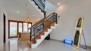 Un interno moderno con pavimento lucido, una scala con gradini in legno e ringhiere nere, una zona cucina e un grande specchio.