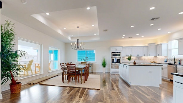 A spacious kitchen with a central island, white cabinetry, and a dining area with wooden chairs and a rug. - KD694 Private Heated Pool, Ocean Views (Port Aransas)