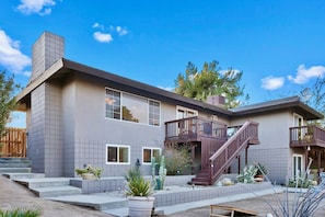 A two-story house with a balcony, a chimney, and a staircase leading to the upper floor. - Indigo Sky Oasis: Pool, Hot Tub, Near Joshua Tree (Yucca Valley)
