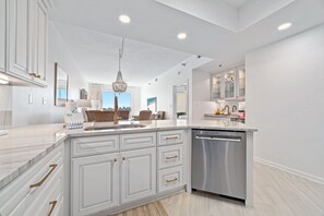 A modern kitchen with white cabinetry, a stainless steel dishwasher, and a large island with a sink. - Waterfront Condo w/ Boat Slip, Lift, Pools & Cove Views | BEACHBALL PROPERTIES (Orange Beach)