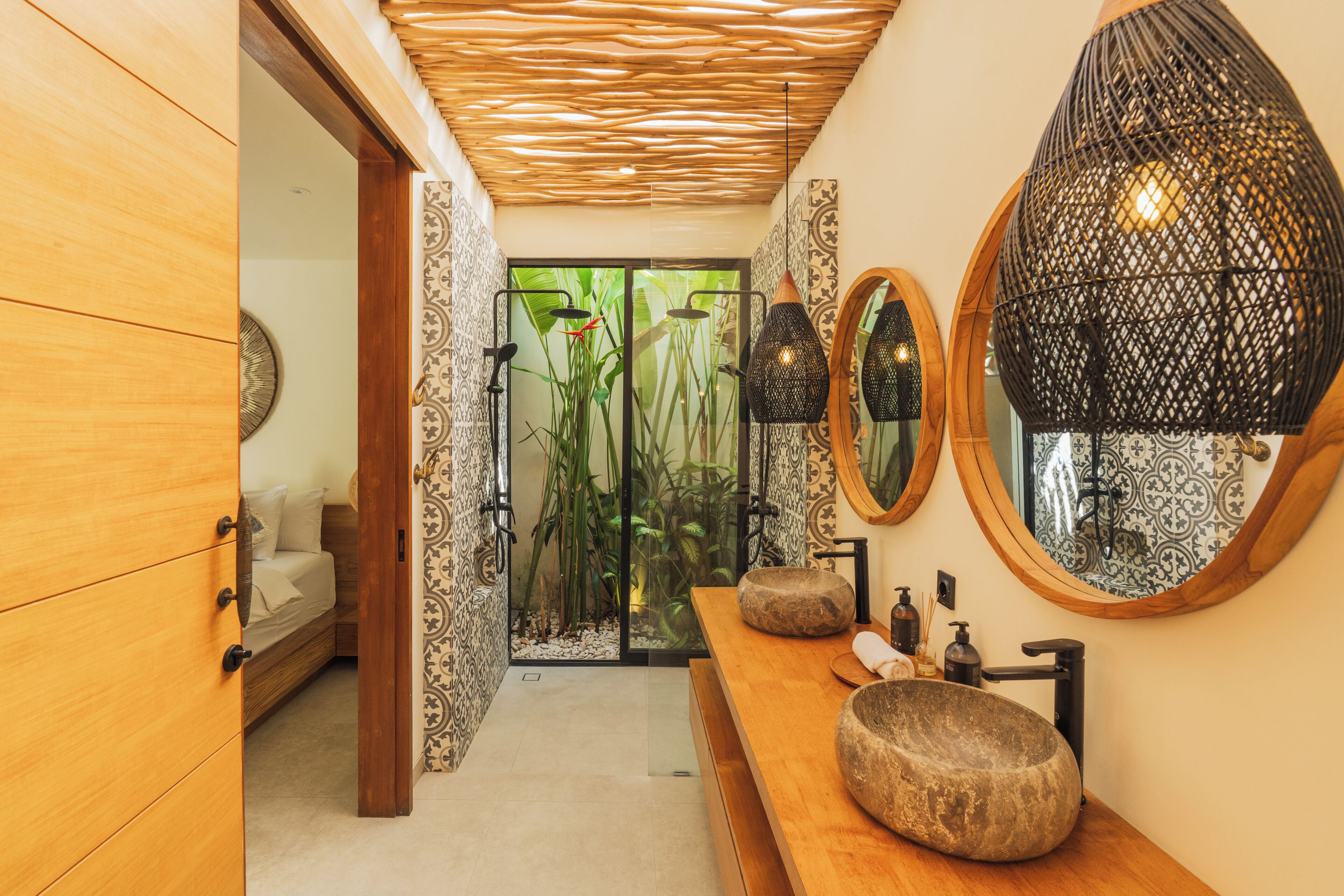 A bathroom with a wooden vanity, a stone basin, a mirror, and a shower area with plants.