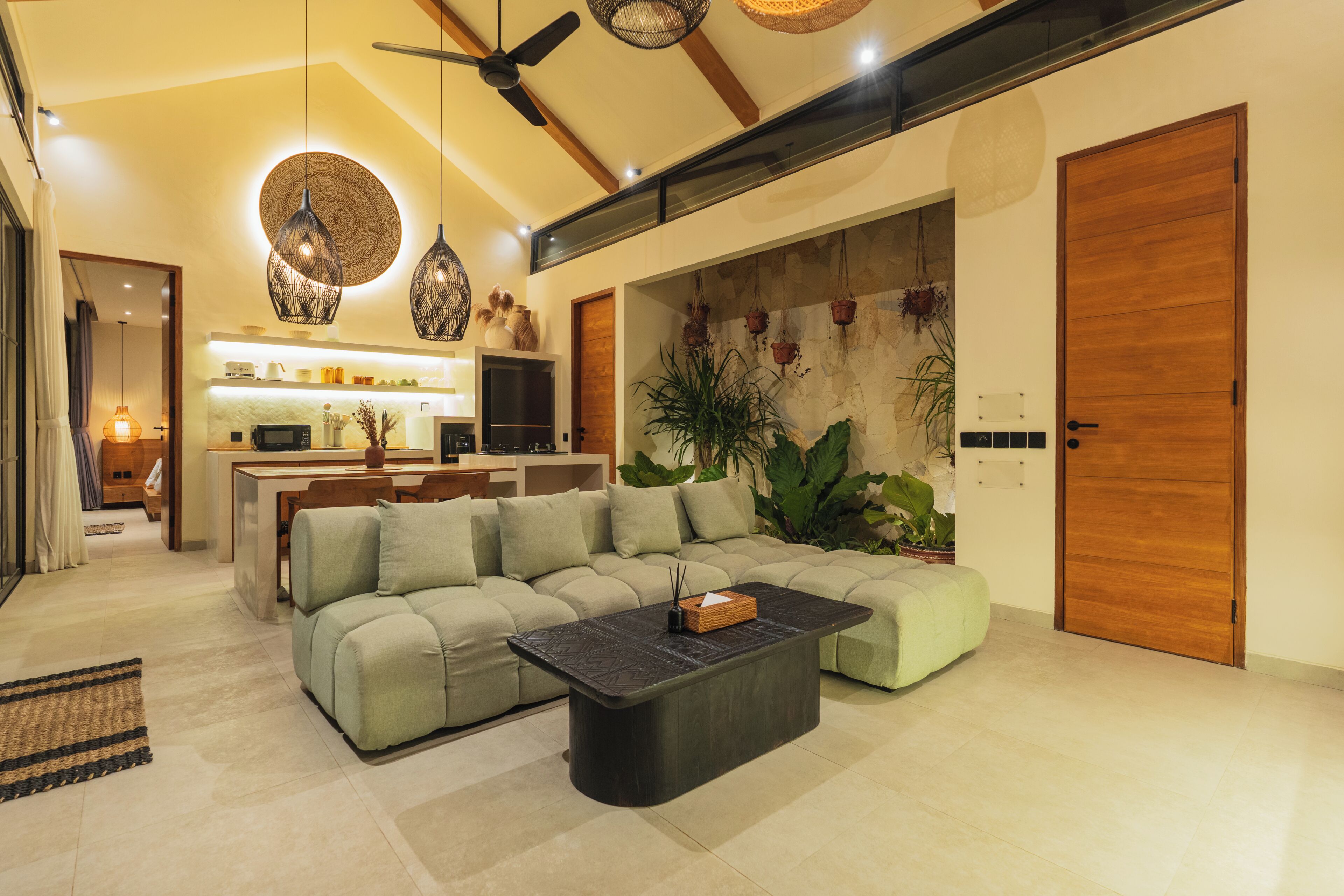 A modern living room with a sectional sofa, a coffee table, and a dining area with a kitchen in the background.