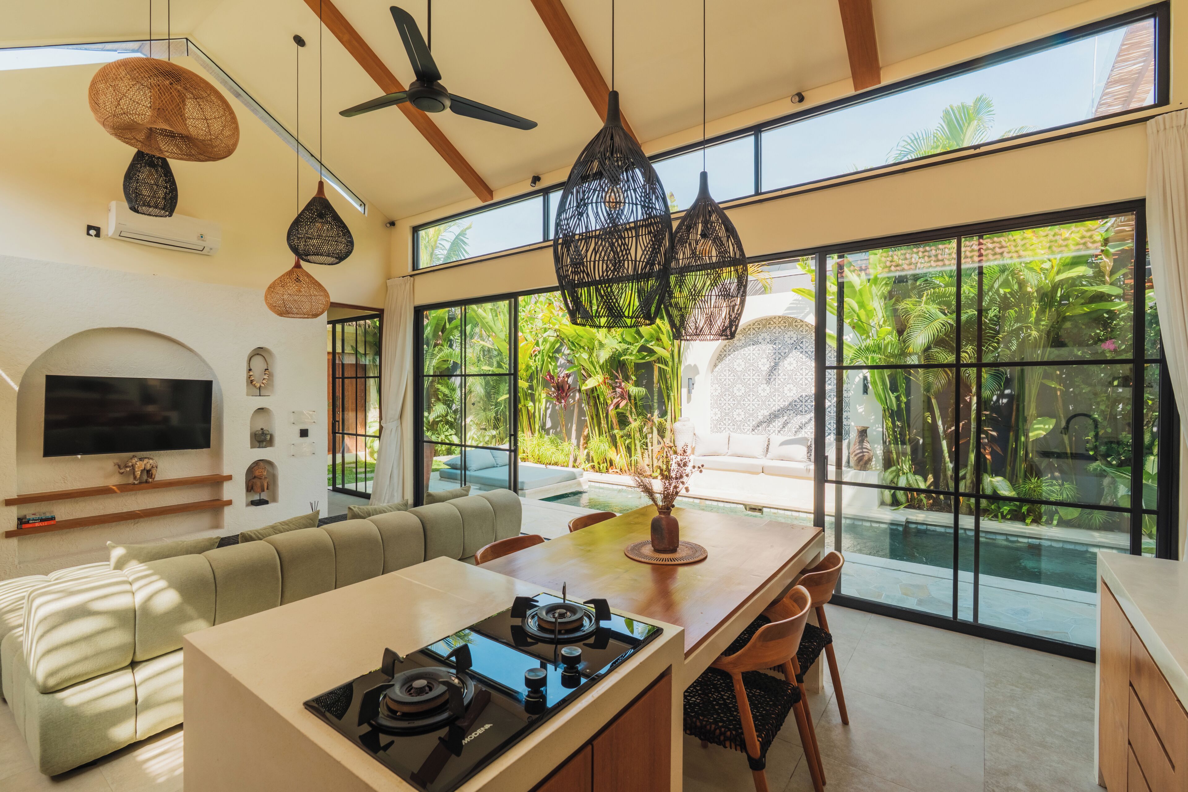 A modern kitchen with a central island, dining area, and a large window with a view of greenery.