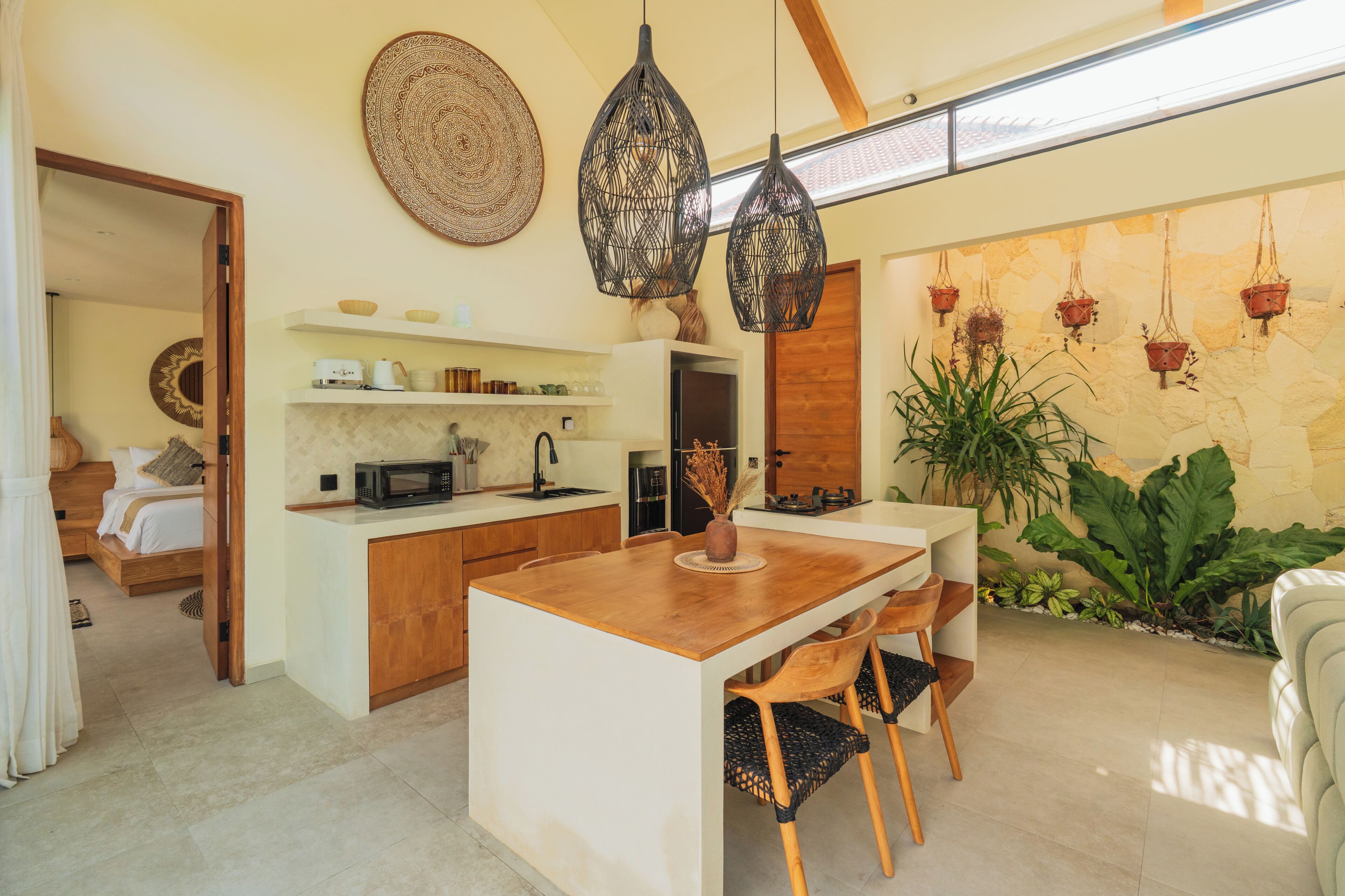 Una cocina moderna con una isla central, luces colgantes y una pared de piedra con macetas colgantes.