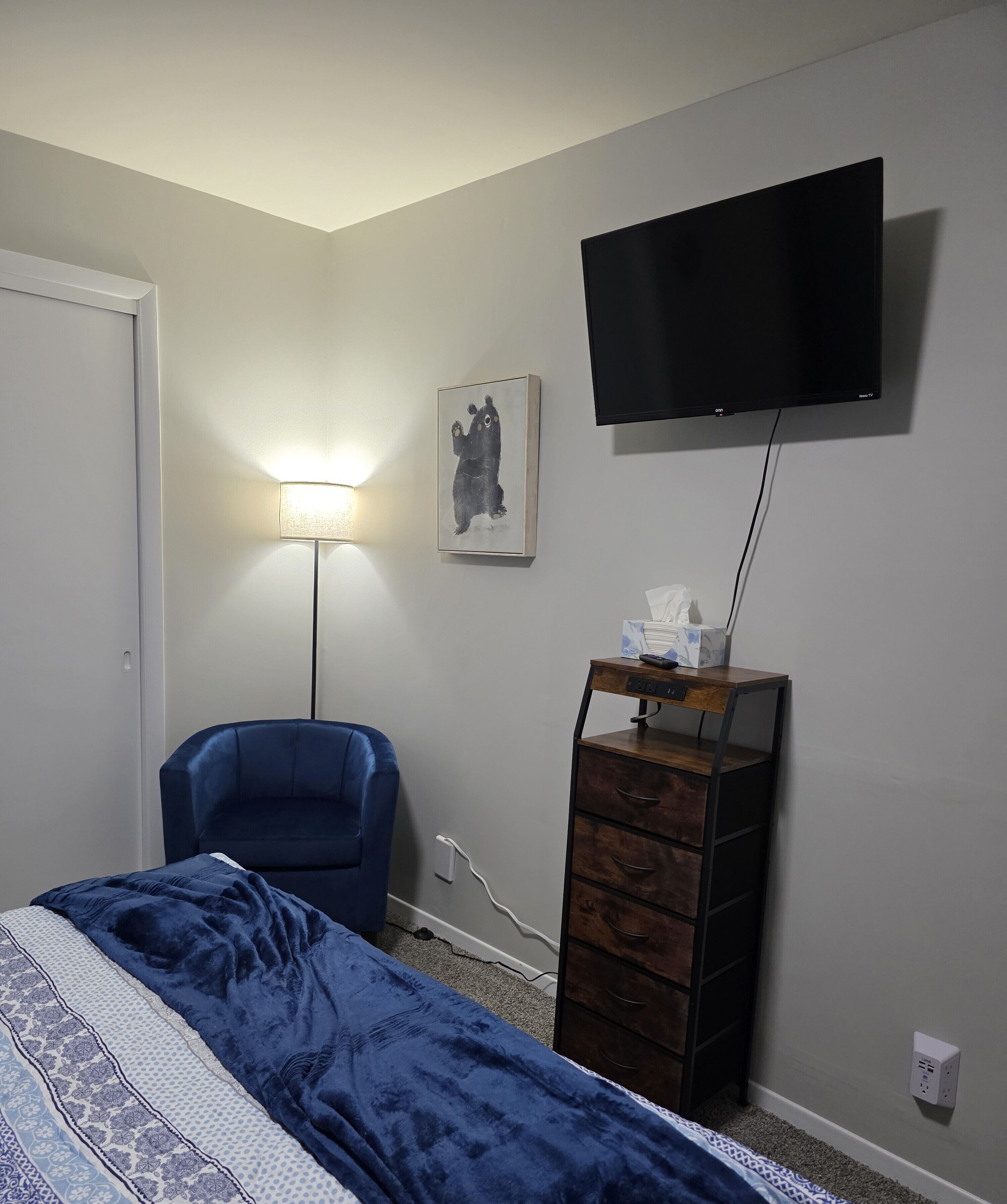 A bedroom with a bed, a chair, a dresser, a TV, and a lamp.