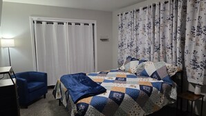 A bedroom with a bed, a blue chair, a desk, and a lamp.