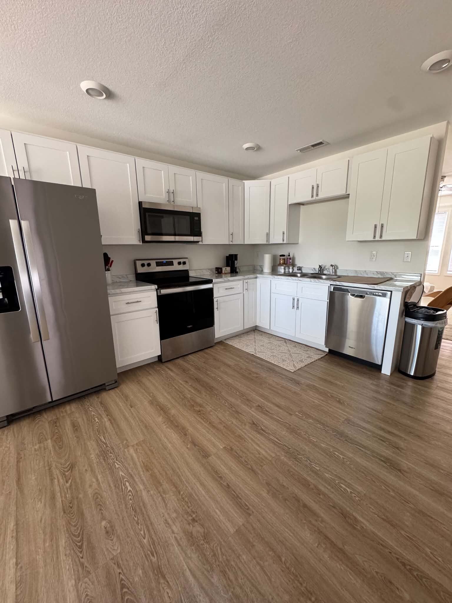 A modern kitchen with white cabinets, stainless steel appliances, and a wooden floor.