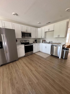 Une cuisine moderne avec des meubles blancs, des appareils en acier inoxydable et un plancher en bois.
