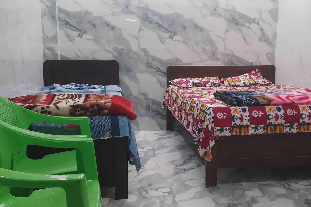 Una habitación con dos camas, una silla de plástico verde y una ventana.