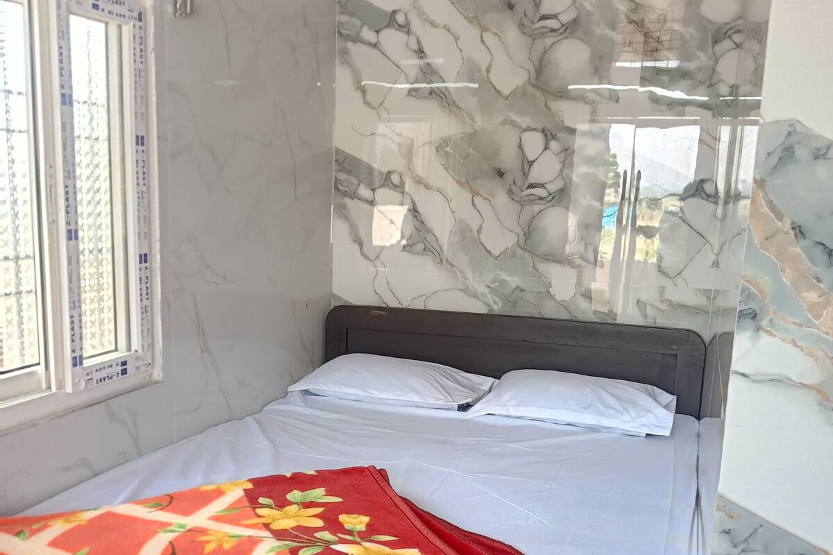 Una cama con una manta estampada con motivos florales, una pared con diseño de mármol y una ventana con persianas.
