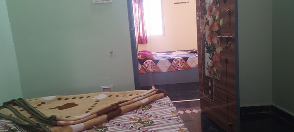A bedroom with a bed covered by a patterned blanket, a wardrobe, and a window with curtains. - SRLN Residency (Mantralayam)
