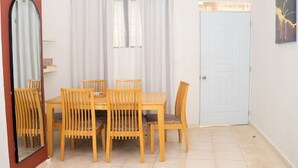 Una zona pranzo con tavolo e sedie in legno, una tenda bianca, una porta e uno specchio.
