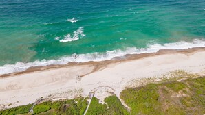 Vista aérea de uma praia com águas turquesa cristalinas, areal e vegetação rala.