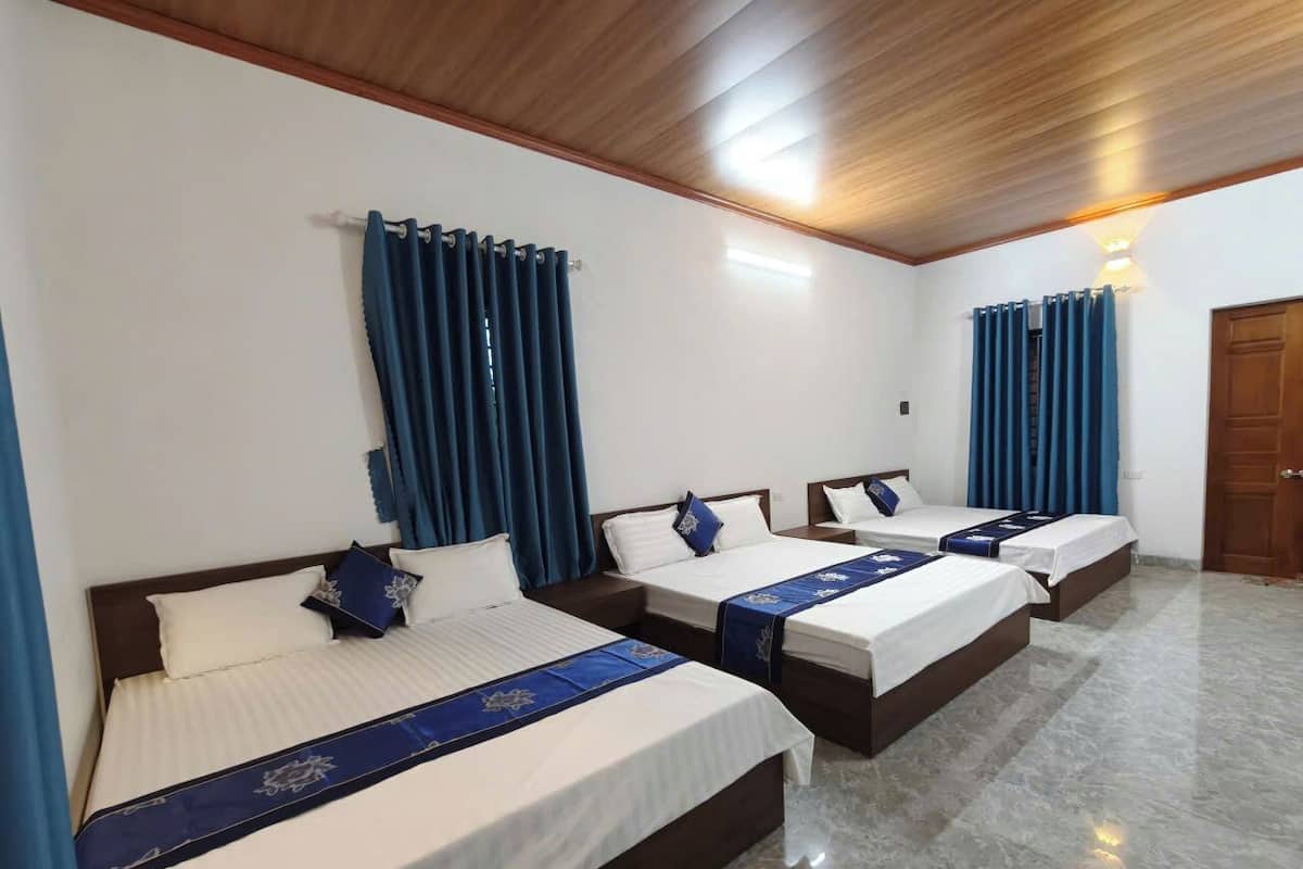 A hotel room with three beds, wooden headboards, and blue curtains.