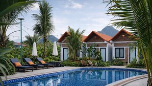 A swimming pool with lounge chairs and umbrellas, surrounded by lush greenery and a mountain backdrop. - Senna Garden HomeStay (Hoa Lu)