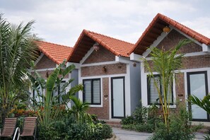 A modern building with a brick facade and red-tiled roofs. There are large windows and doors, and the building is surrounded by lush greenery and plants. - Senna Garden HomeStay (Hoa Lu)